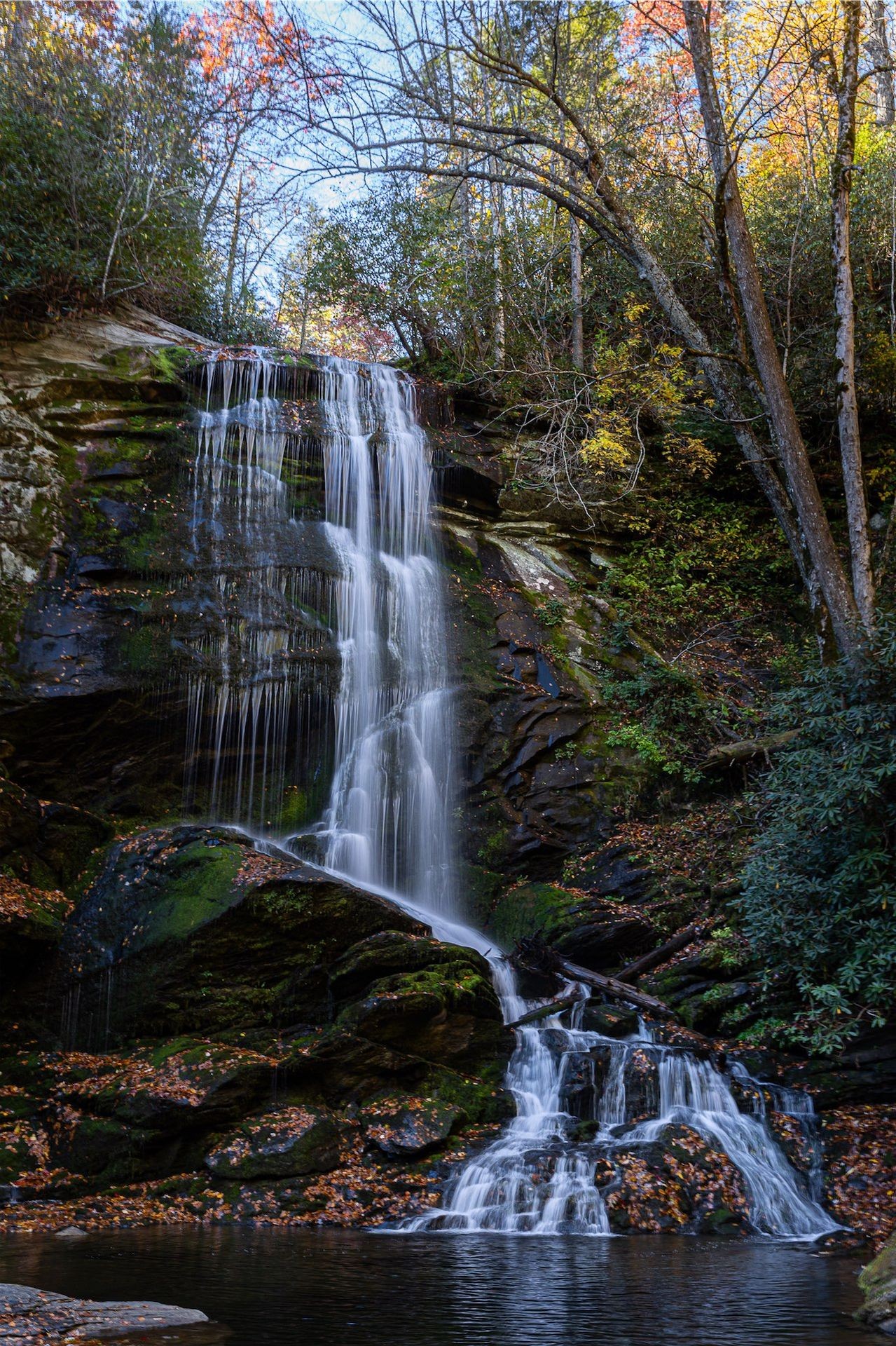Waterfall cascading over moss-covered rocks surrounded by autumn foliage.
