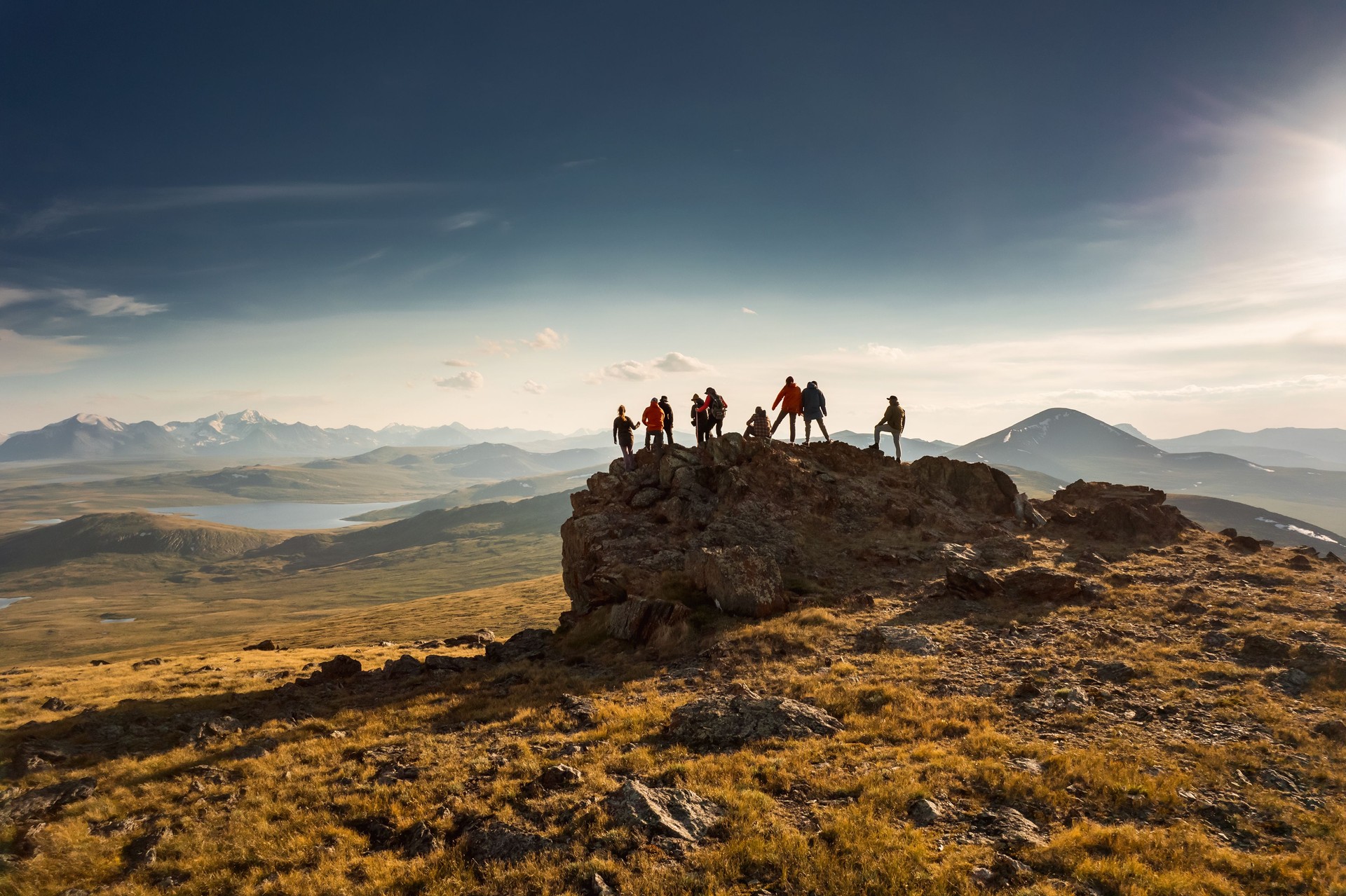 Big group of hikers stands at mountain top and looks at sunset